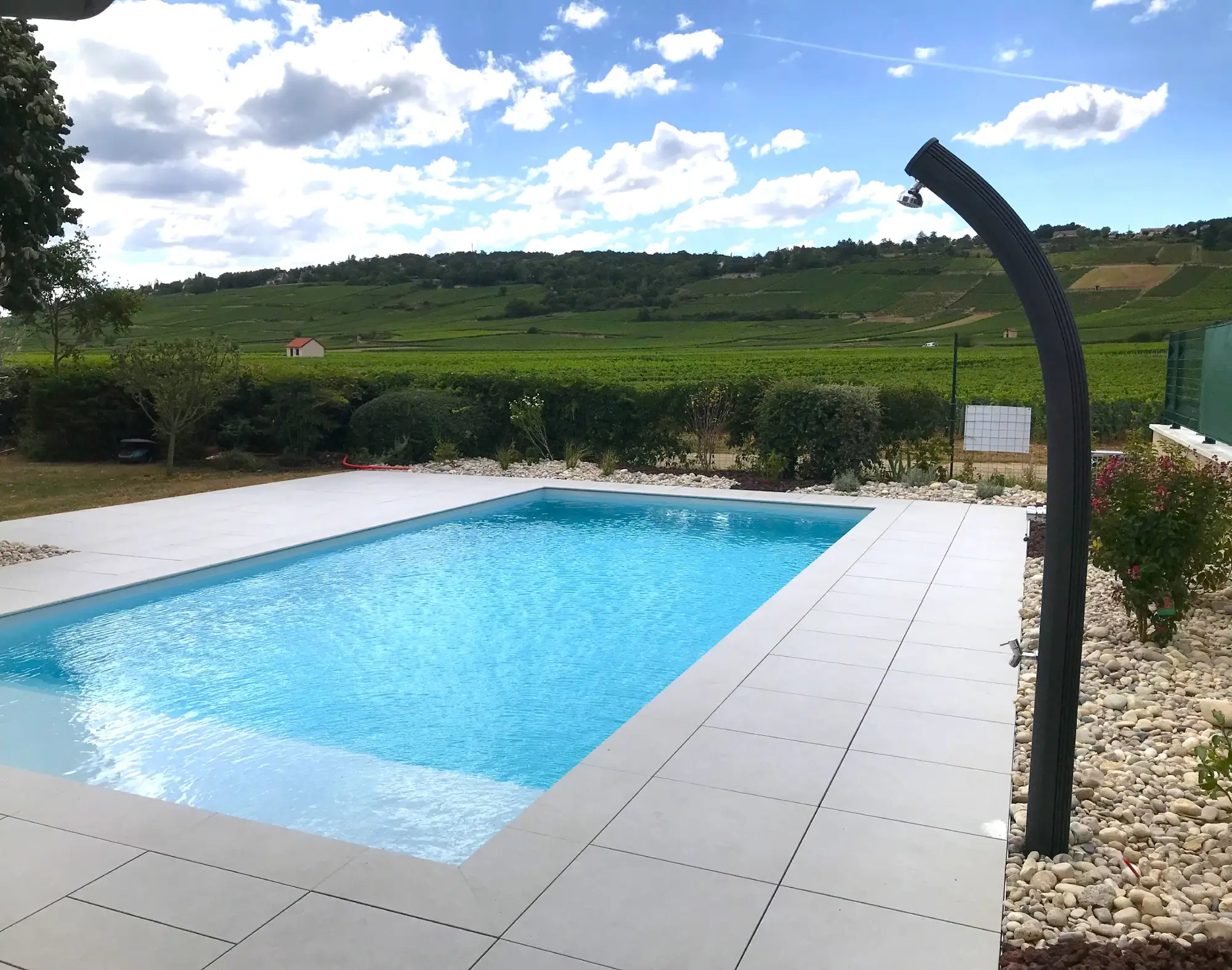 Piscine et terrasse en pierre claire avec douche extérieure et vue sur le vignoble — Beaune, Côte-d’Or — Perret Paysage & Piscine